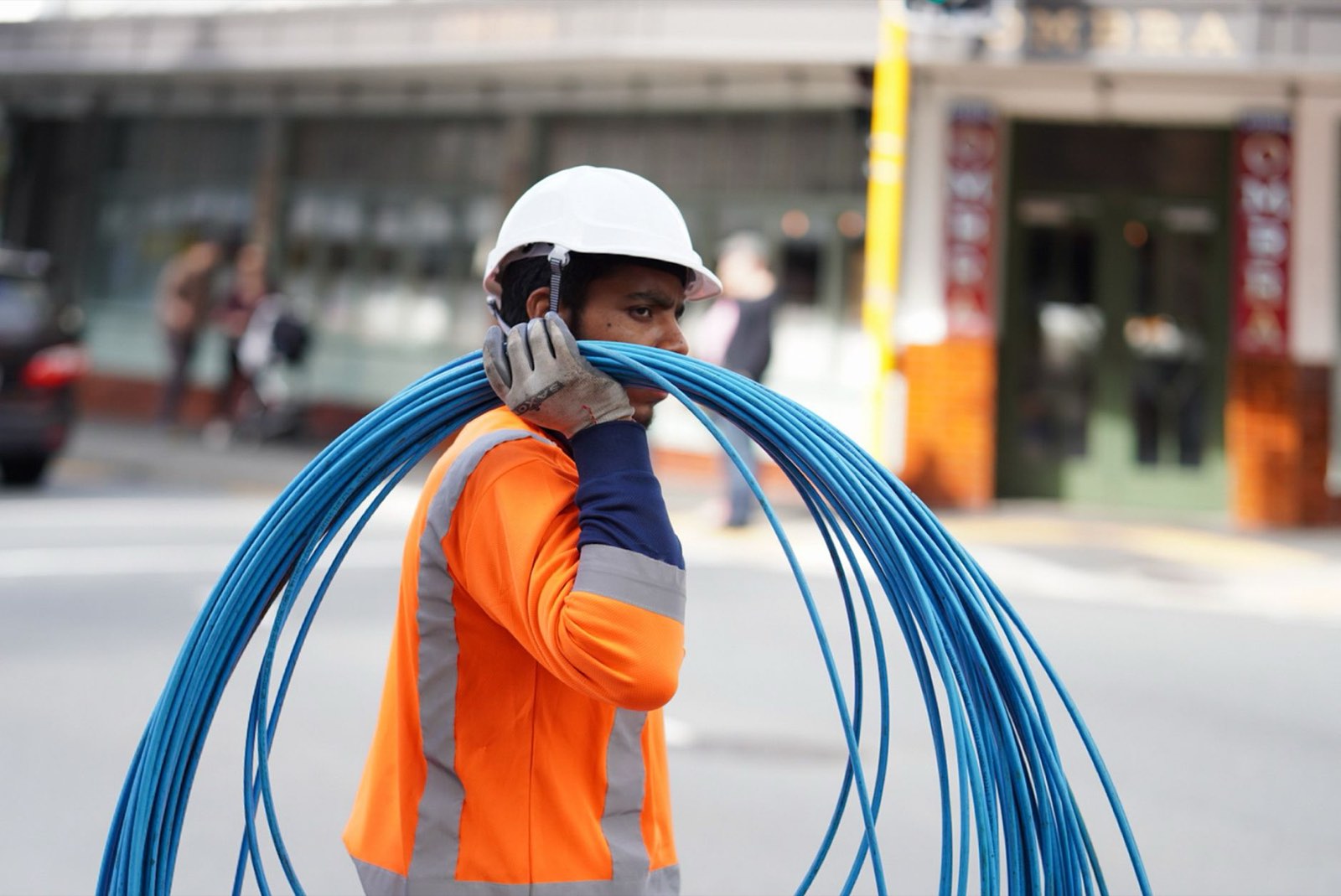 Técnico de campo com capacete e colete refletivo carregando um rolo de cabo de rede azul no ombro