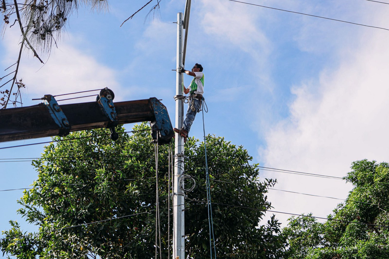 Técnico de campo com cinturão de segurança trabalhando no alto de um poste de rede